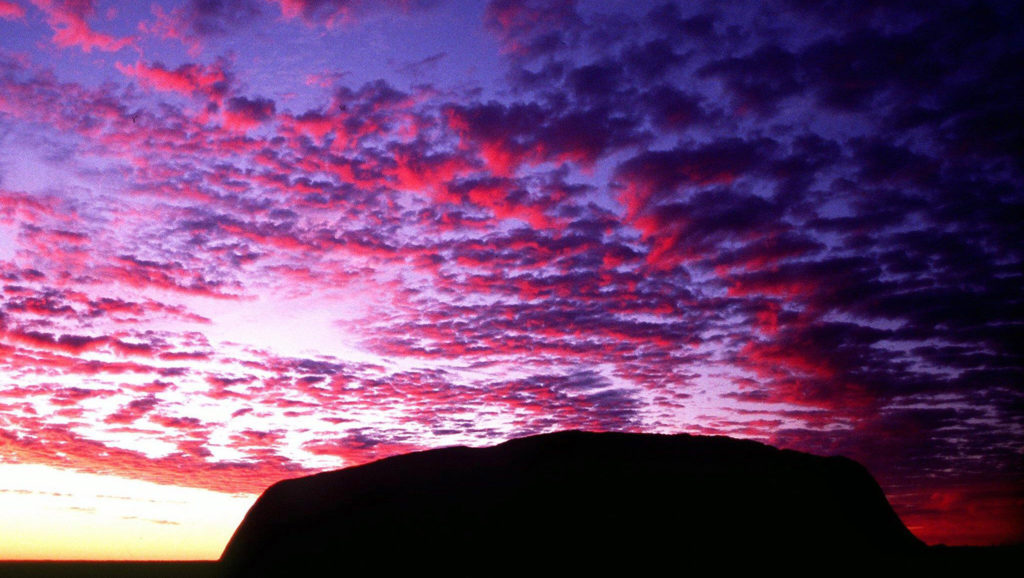 Η δύση του ήλιου πάνω από το Ουλουρούgoes with"AUSTRALIA-TOURISM" SYD98 - 19910525 - ULURU-KATA TJUTA, AUSTRALIA : (FILES) A file photo dated 25 May 1991 of sunrise over Uluru (Ayer's Rock), the largest single rock monolith in the world, in central Australia which UNESCO accorded World Heritage listing in 1987. According to the manager of Uluru Kata-Tjuta national park, 07 March 2003, thousands of packages containing rocks or soil from Uluru have been mailed back over the years by foreign and Australian tourists alike beset by serious misfortune or simple remorse. Most of those returning pieces of the rock complain of suffering misfortune they believe linked to their crime. Uluru is one of the most sacred sites for Australia's indigenous Aborigines and is the country's best known natural monument. (FILM) EPA PHOTO FILES AFP TORSTEN BLACKWOOD tb/re/ta-vl