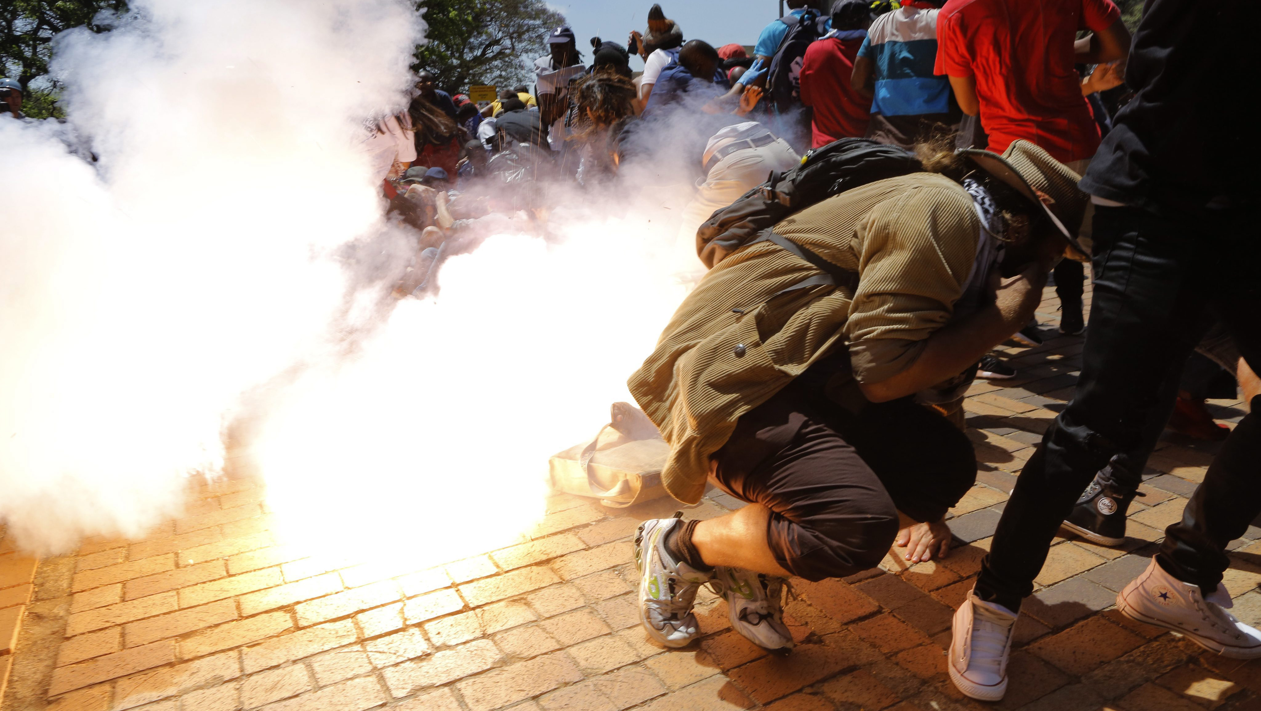 epaselect epa05579630 Students from Wits University fall to the ground as a police thunder flash explodes amongst them during ongoing protests against the cost of higher education in Johannesburg, South Africa, 10 October 2016. The ministry of education announced a 8 percent increase of university fees following calls by student demonstrators of a 0 percent increase. The violent protests have spread to many of the countries higher education campuses and have been ongoing for several weeks. EPA/KIM LUDBROOK
