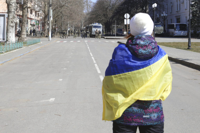 Γυναίκα τυλγιμένη με την ουκρναική σημαία μπροστά από ρωσικές δυνάμεις