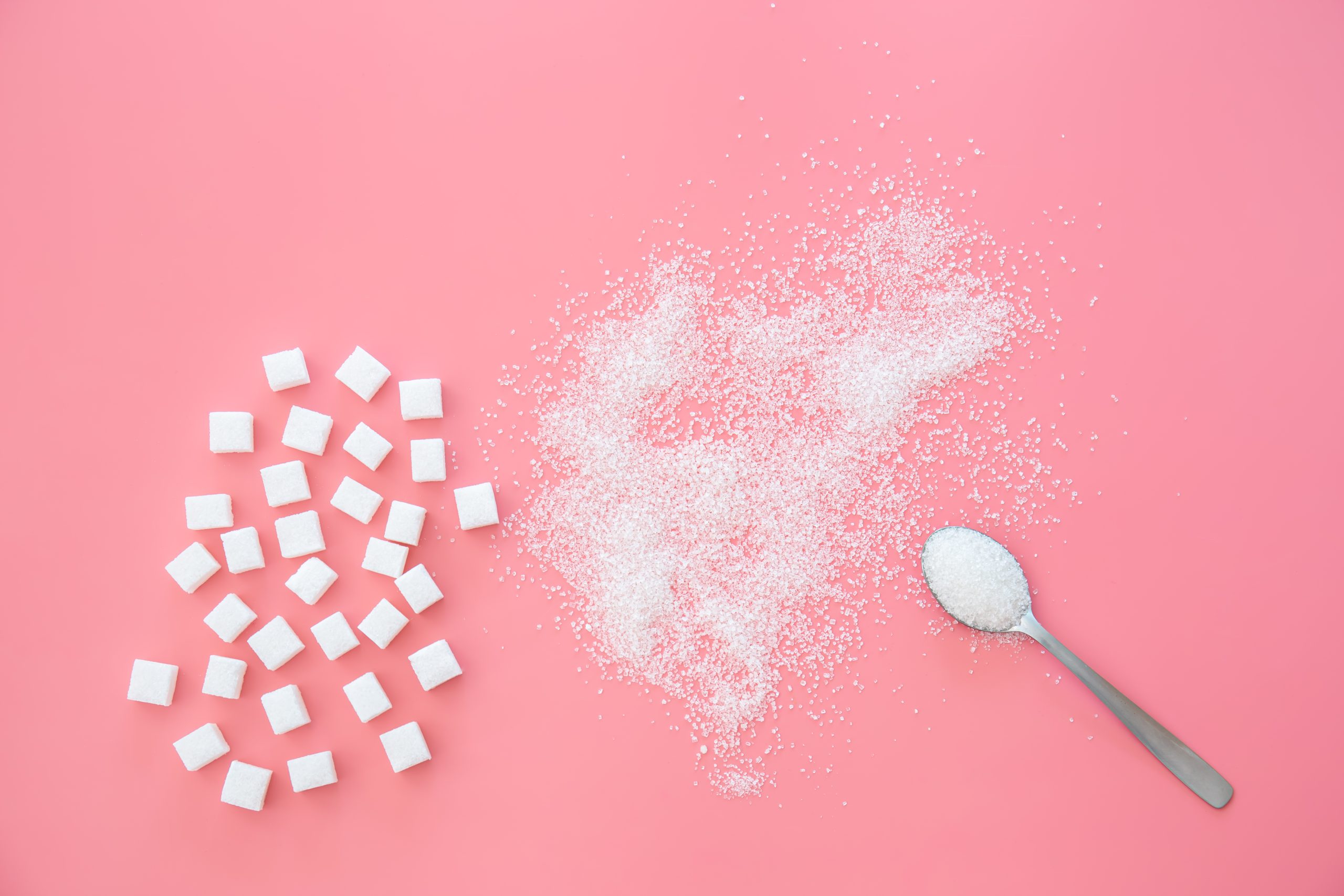 Scattered sugar and sugar cubes on a pink background, flat lay.